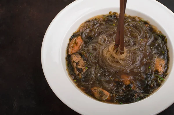 Japanese cuisine, soup with chashu pork, chives, sprouts, noodles and seaweed on the table under the sunlight. Old black rustic background. Top view