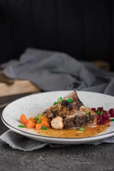 Revbensspjäll med rödbetor, morötter, stekt svamp och sås på en vit platta. Restaurang som serverar. Gammal svart rustik bakgrund. Ovanifrån — Stockfoto