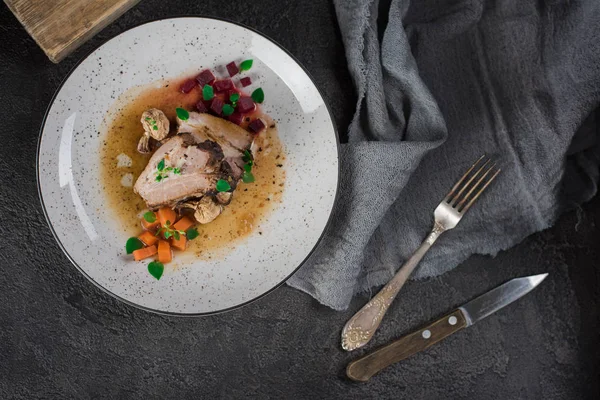 Costillas de cerdo con remolacha, zanahorias, champiñones fritos y salsa en un plato blanco. Servicio de restaurante. Fondo rústico negro viejo. Vista superior —  Fotos de Stock