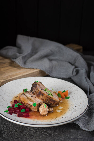 Pork ribs with beets, carrots, fried mushrooms and sauce on a white plate. Restaurant serving. Old black rustic background. Top view