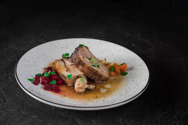 Costillas de cerdo con remolacha, zanahorias, champiñones fritos y salsa en un plato blanco. Servicio de restaurante. Fondo rústico negro viejo. Vista superior —  Fotos de Stock