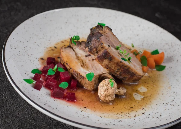 Schweinerippchen mit Rüben, Karotten, gebratenen Pilzen und Soße auf einem weißen Teller. Restaurant serviert. alten schwarzen rustikalen Hintergrund. Ansicht von oben — Stockfoto