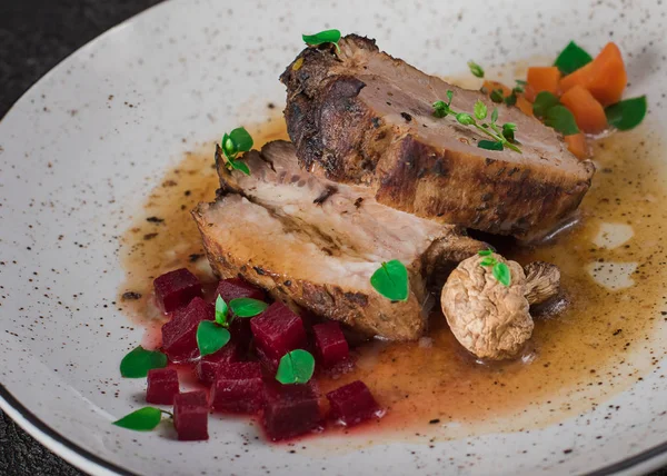 Schweinerippchen mit Rüben, Karotten, gebratenen Pilzen und Soße auf einem weißen Teller. Restaurant serviert. alten schwarzen rustikalen Hintergrund. Ansicht von oben — Stockfoto