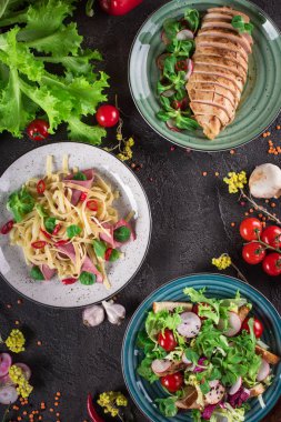 Lezzetli yemek. İtalyan makarna, taze sebze salatası ve siyah arka plan üzerine kavrulmuş tavuk göğsü. Sağlıklı gıda. Yakın çekim. Üstten Görünüm