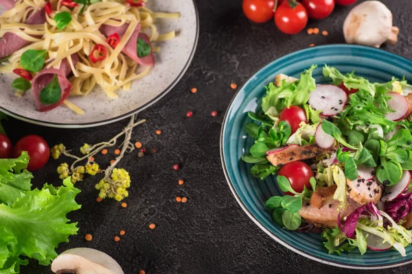 Delicioso jantar. Massa italiana e salada de legumes frescos no fundo preto. Comida saudável. Fecha. Vista superior — Fotografia de Stock