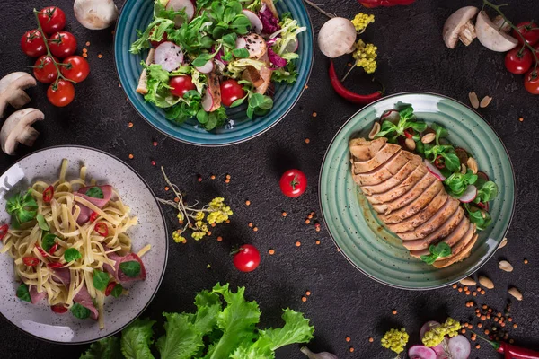 Délicieux dîner. Pâtes italiennes, salade de légumes frais et poitrine de poulet rôtie sur fond noir. Une nourriture saine. Ferme là. Vue du dessus — Photo