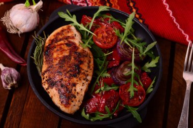 Roka ve siyah bir tavada sebze yeşil salata ile ızgara tavuk göğsü. Ahşap rustik arka plan. Üstten Görünüm