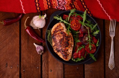 Roka ve siyah bir tavada sebze yeşil salata ile ızgara tavuk göğsü. Ahşap rustik arka plan. Üstten Görünüm