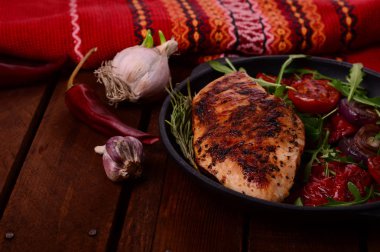 Roka ve siyah bir tavada sebze yeşil salata ile ızgara tavuk göğsü. Ahşap rustik arka plan. Üstten Görünüm