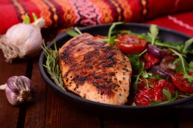 Roka ve siyah bir tavada sebze yeşil salata ile ızgara tavuk göğsü. Ahşap rustik arka plan. Üstten Görünüm