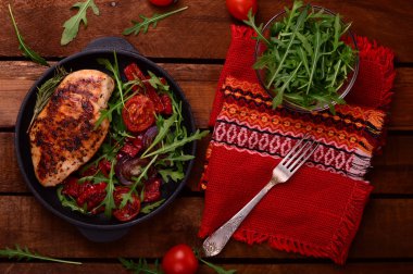 Roka ve siyah bir tavada sebze yeşil salata ile ızgara tavuk göğsü. Ahşap rustik arka plan. Üstten Görünüm