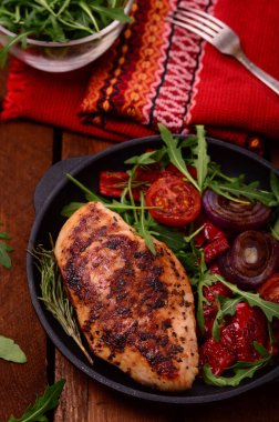 Roka ve siyah bir tavada sebze yeşil salata ile ızgara tavuk göğsü. Ahşap rustik arka plan. Üstten Görünüm