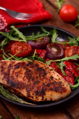 Roka ve siyah bir tavada sebze yeşil salata ile ızgara tavuk göğsü. Ahşap rustik arka plan. Üstten Görünüm