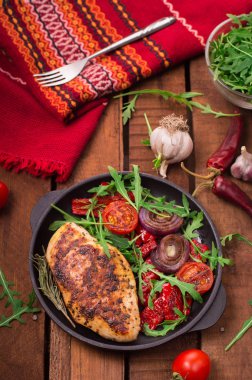 Roka ve siyah bir tavada sebze yeşil salata ile ızgara tavuk göğsü. Ahşap rustik arka plan. Üstten Görünüm