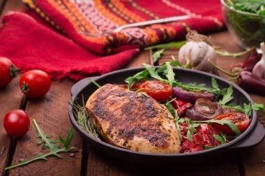 Roka ve siyah bir tavada sebze yeşil salata ile ızgara tavuk göğsü. Ahşap rustik arka plan. Üstten Görünüm