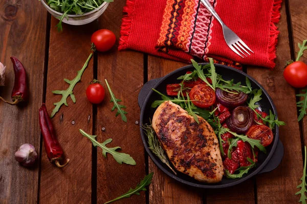 Roka ve siyah bir tavada sebze yeşil salata ile ızgara tavuk göğsü. Ahşap rustik arka plan. Üstten Görünüm