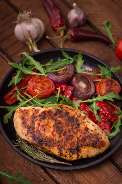 Roka ve siyah bir tavada sebze yeşil salata ile ızgara tavuk göğsü. Ahşap rustik arka plan. Üstten Görünüm