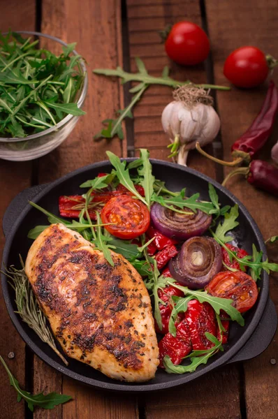 Roka ve siyah bir tavada sebze yeşil salata ile ızgara tavuk göğsü. Ahşap rustik arka plan. Üstten Görünüm