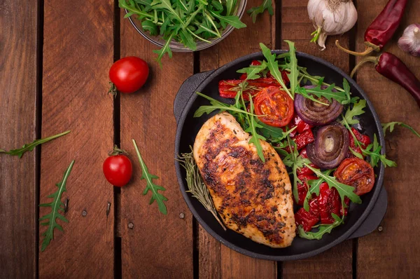 Peito de frango grelhado com salada verde de arugula e verduras em uma panela preta. Fundo rústico de madeira. Vista superior — Fotografia de Stock