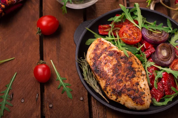 Roka ve siyah bir tavada sebze yeşil salata ile ızgara tavuk göğsü. Ahşap rustik arka plan. Üstten Görünüm