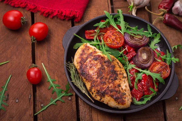 Roka ve siyah bir tavada sebze yeşil salata ile ızgara tavuk göğsü. Ahşap rustik arka plan. Üstten Görünüm