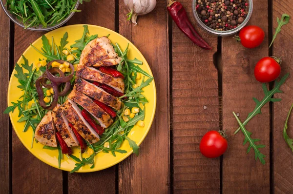 Peito de frango grelhado com salada verde de rúcula e verduras em uma chapa amarela. Fundo rústico de madeira. Vista superior — Fotografia de Stock