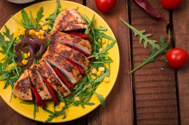 Roka ve sarı bir tabakta sebze yeşil salata ile ızgara tavuk göğsü. Ahşap rustik arka plan. Üstten Görünüm