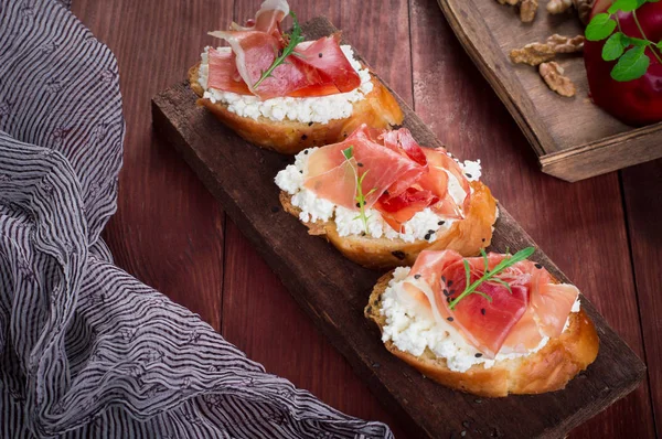 Baguette com queijo de casa de campo, arugula e presunto, sanduíche em uma tábua, foco seletivo. Fundo rústico de madeira. Vista superior — Fotografia de Stock