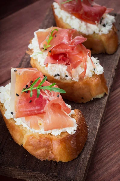 Baguette with cottage cheese, arugula and ham, sandwich on a board, selective focus. Wooden rustic background. Top view