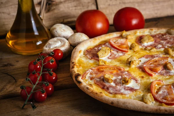 Pizza inteira com frango, presunto e tomate na mesa de madeira com ingredientes — Fotografia de Stock