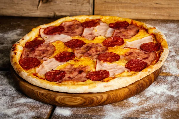 Pizza com presunto e salsichas sobre fundo de madeira — Fotografia de Stock