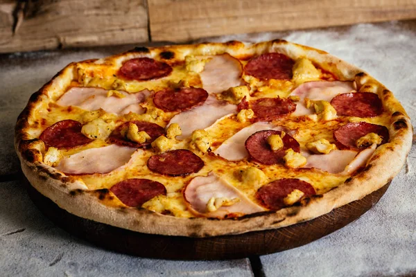 Pizza com presunto, salsichas e frango sobre fundo de madeira — Fotografia de Stock