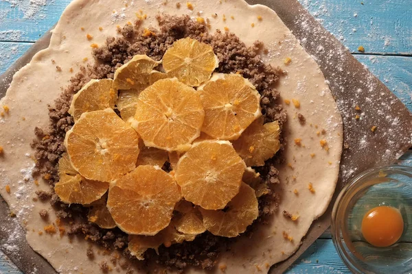 Galette těsta s ořechy a oranžové na pečicím papírem na modrém pozadí — Stock fotografie