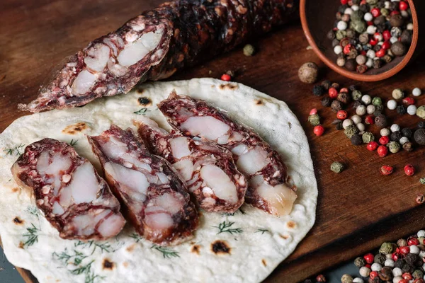 Smoked salami with pita and spices on a wooden cutting board on dark background — Stock Photo, Image