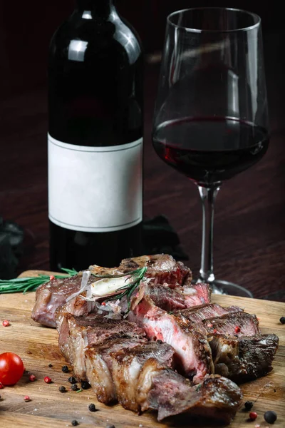 Rebanadas a la parrilla T-bone filete tomates en una tabla de cortar con botella de vino y vino sobre fondo oscuro — Foto de Stock