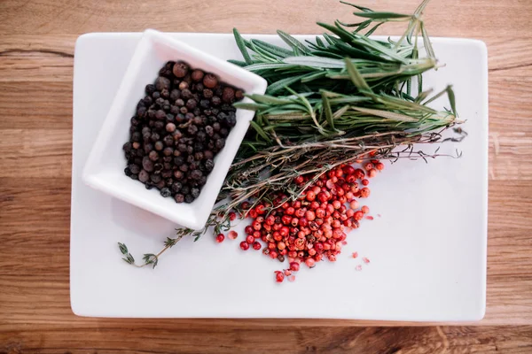 Rosemary ile siyah ve pembe biber mısır ahşap arka plan üzerinde beyaz bir tabakta. Üstten Görünüm 