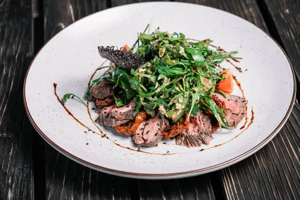 Sıcak Dana salatası, kurutulmuş domates ve koyu ahşap arka plan üzerinde roka