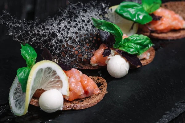 Salmon tartare with rye bread toasts on black plate on dark wood background — Stok Foto
