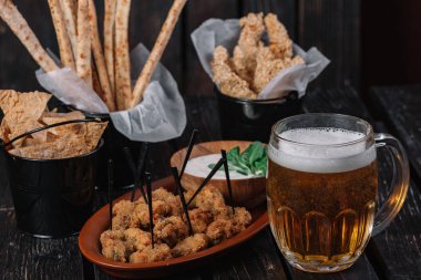 Kupa bira ve koyu ahşap arka plan snacks. Grisini, ızgara tavuk göğsü, pide cips, kızarmış tavuk Kalpler, sos