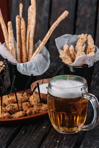 Kupa bira ve koyu ahşap arka plan snacks. Grisini, ızgara tavuk göğsü, pide cips, kızarmış tavuk Kalpler, sos