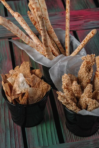 Snacks for beer on dark wood background. Grissini, chicken grilled breast, pita chips