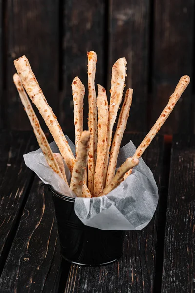 Snacks for beer on dark wood background. Grissini in a black small bucket