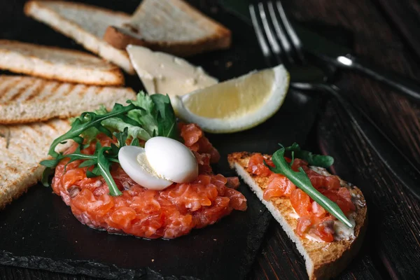 Close-up of salmon tartare served with quail egg, butter, bread — Stock Photo, Image