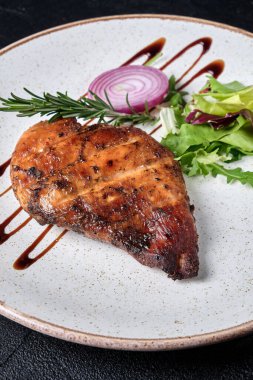 Beyaz tabakta salata ve soğanlı ızgara tavuk filetosu. Siyah beton arkaplan