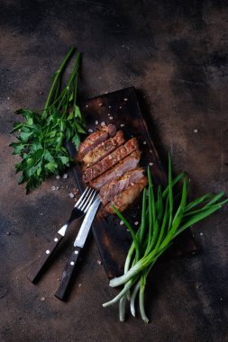 Maydanozlu ve pırasalı ızgara et. Kesme tahtası ve koyu arkaplanda çatal bıçak takımı. Üst görünüm