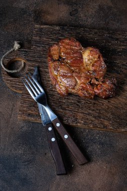 Kesme tahtasında ızgara et ve arka planda çatal bıçak takımı. Üst görünüm