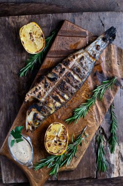 Izgara alabalık kesim tahtasında servis edilir. Ahşap arka planda. Üst görünüm