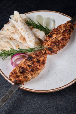 Izgara et şişi, şiş kebap ve beyaz tabakta pide, siyah arka planda soğan. Gürcistan mutfağı kavramı. Et ve baharattan yapılmış sulu lula kebabı.