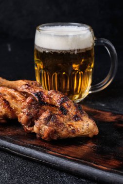 Bir bardak bira, ızgara tavuk kanadı ve koyu beton arka planda domates sosu.