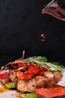 Kızarmış dana etine bir damla kiraz sosu dökülüyor. Karanlık bir arka planda